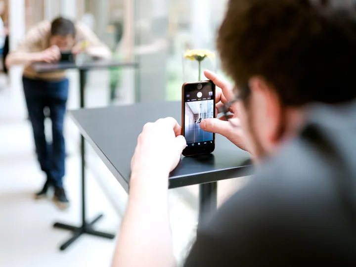 Teilnehmer fotografiert im Workshop mit dem Smartphone eine Szene am Stehtisch